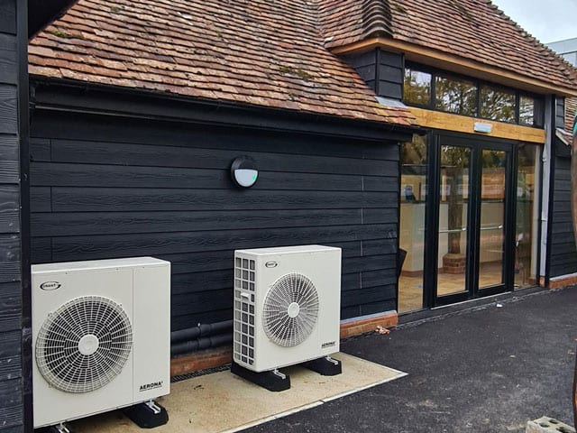 Two air source heat pump units installed against a black timber clad building